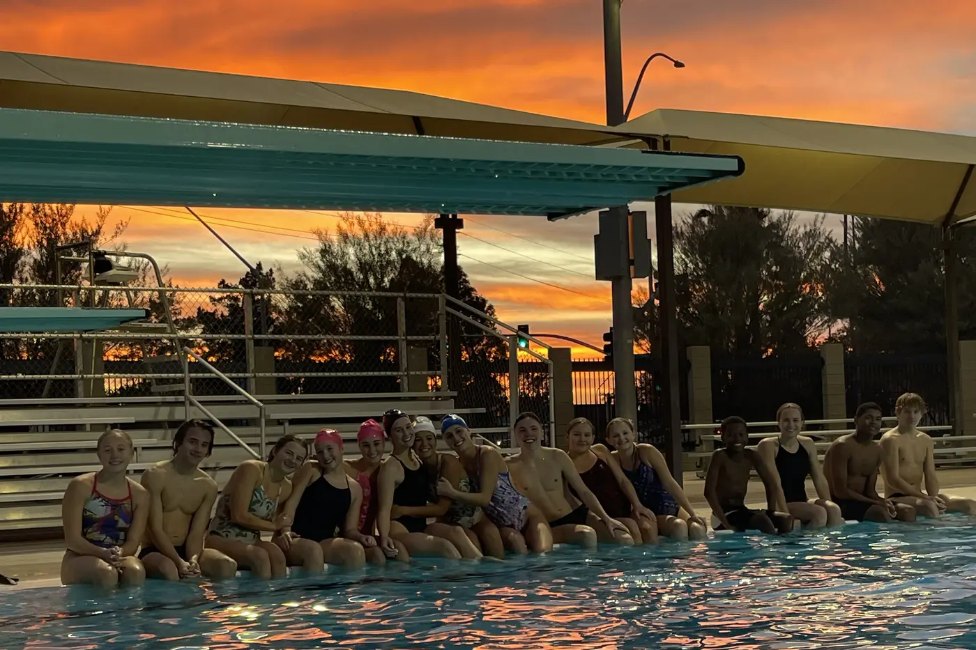 The team sitting along the edge of the pool under a burning orange sky, the color reflected across the water.