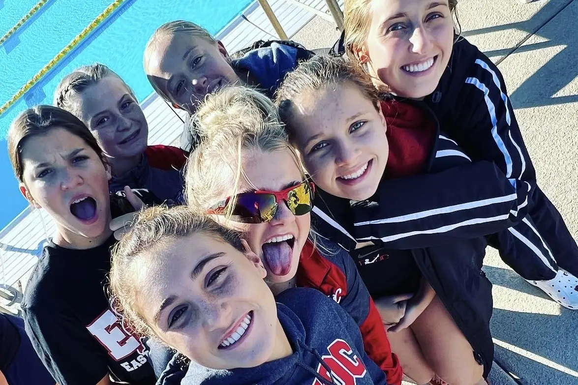 Divers crowded into a group selfie on the pool deck, mid-laugh.