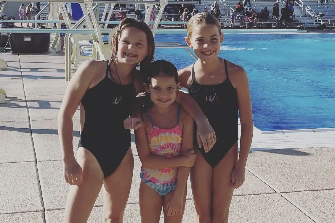 Two divers in team suits poolside with a younger club member between them.