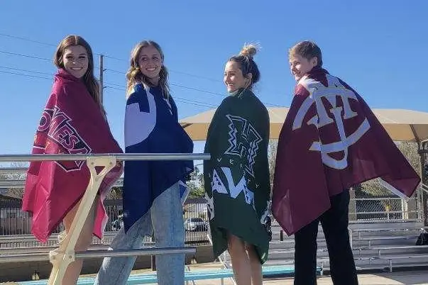 Four divers on the board deck with towels around their shoulders under a clear sky.
