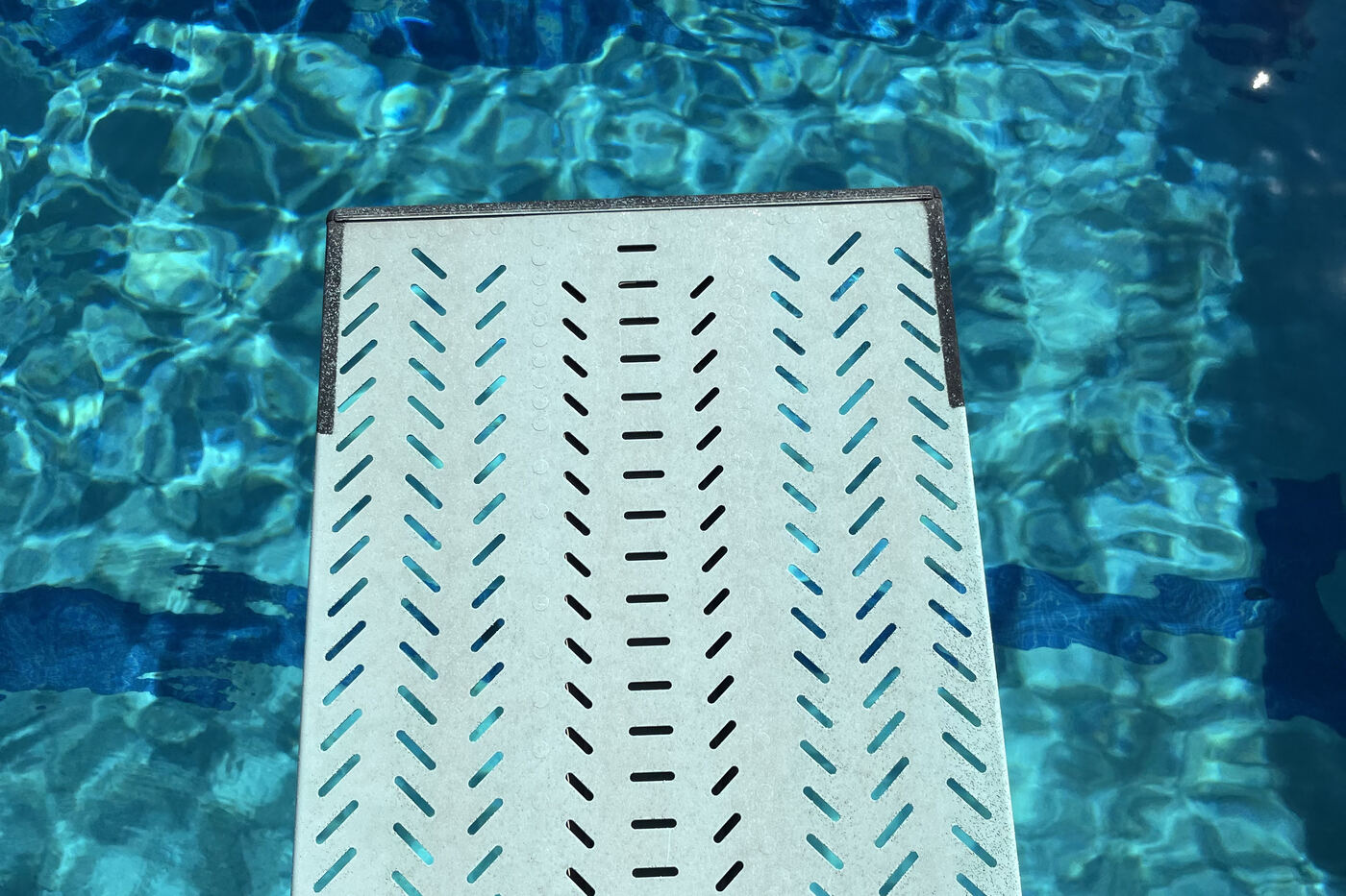 A springboard at Skyline Aquatic Center reaching out over sunlit pool water